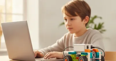 Ребёнок программирует за ноутбуком модель из конструктора, совместимого с WeDo 2.0, — рядом машинка с белым СмартХабом