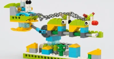 Новогодняя модель «Летающий Санта» из деталей, совместимых с WeDo 2.0: сани с Сантой на голубом рычаге поднялись над двумя оленями и рядом домиков с жёлтыми крышами
