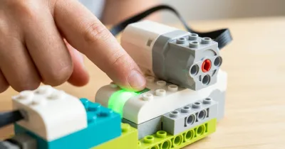 Палец нажимает светящуюся зелёную кнопку смарт-хаба WeDo 2.0 с подключённым мотором