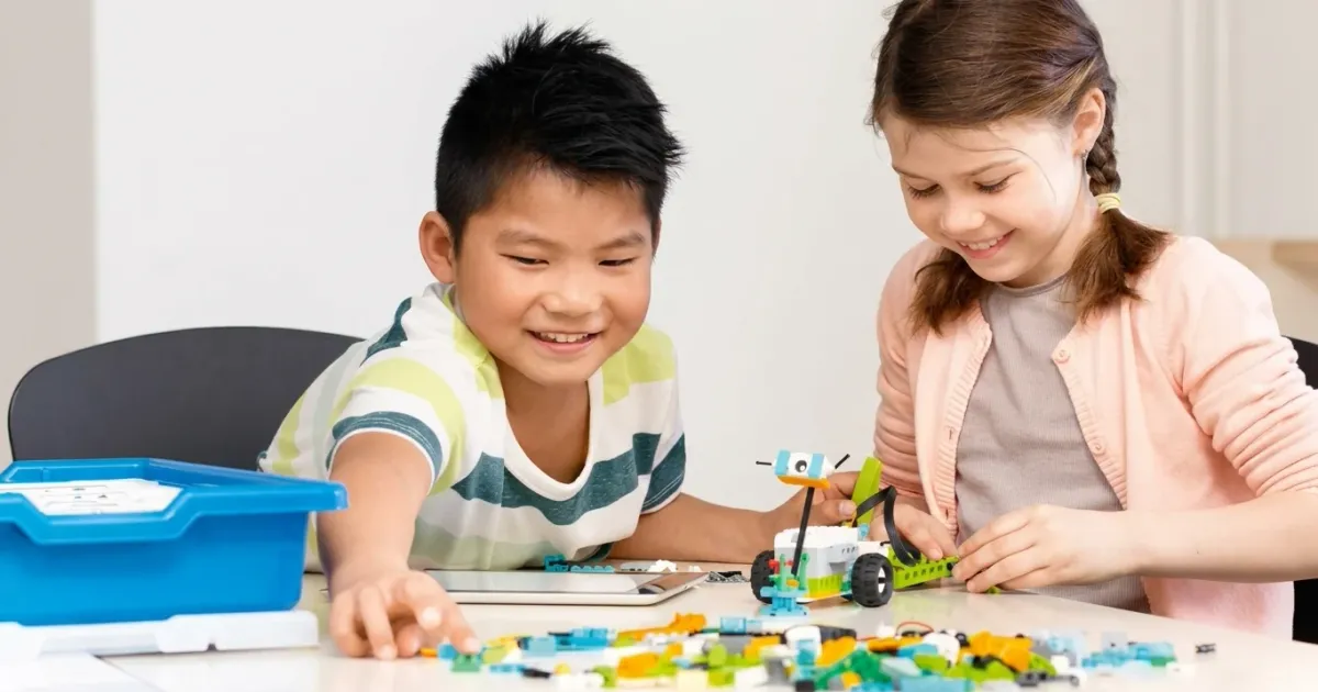 Мальчик и девочка собирают модель из совместимого с WeDo 2.0 конструктора РобоГуру; рядом стоит синяя коробка набора