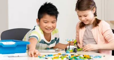 Мальчик и девочка собирают модель из совместимого с WeDo 2.0 конструктора РобоГуру; рядом стоит синяя коробка набора