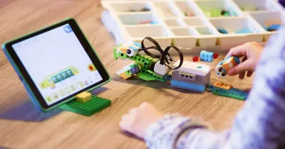 Ребёнок за столом собирает робота из конструктора РобоГуру, совместимого с WeDo 2.0; рядом лежит планшет с приложением