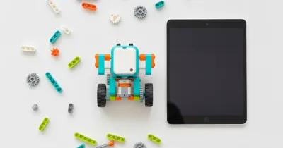 Собранная модель робота из деталей, совместимых с WeDo 2.0; рядом на столе лежат планшет и россыпь деталей